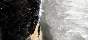 Detail of an art installation by Jennifer Wen Ma. An individual stands in a canyon of paper feathers--black on the left and white on the right