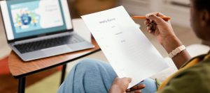 An individual sits in front of a laptop, pencil and paper in hand