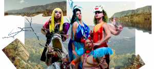 Five colorfully dressed ensemble members from a performance called "TERRITORY: The Island Remembers" pose in shimmering costumes, wigs, and make up. A few give fierce looks to the camera lens standing and kneeling in front of a background of a collage featuring mountains, lush green hills, trees, and other vegetation.