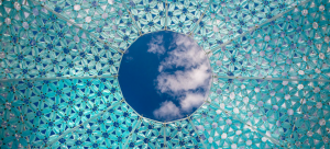 A blue sky with a few whispy white clouds can be seen through a small circle that is the top of a blue patterned Dome Oculus.